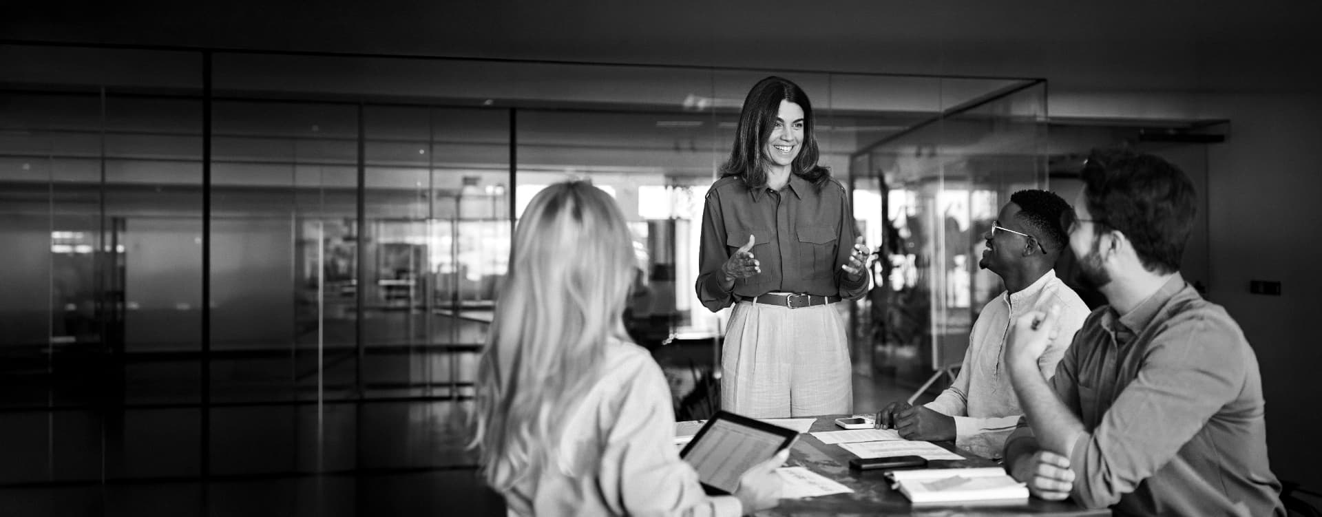 A leader presenting brand traction results to colleagues in a glass-walled meeting room